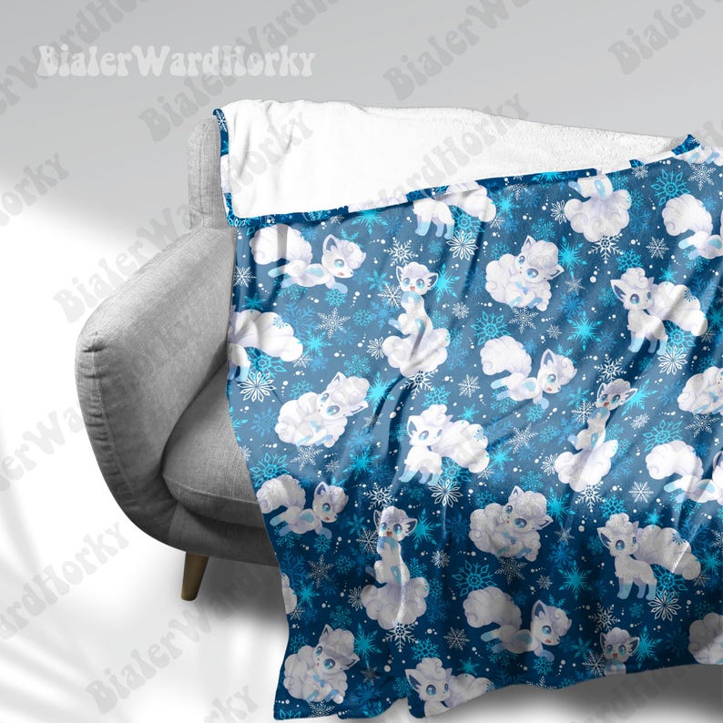 May include: A blue blanket featuring a pattern of white cartoon foxes, clouds, and snowflakes. The blanket is draped over a gray armchair. The top edge of the blanket is white.