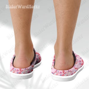 Może przedstawiać: R&oacute;żowe i białe kapcie we wzory z motywem postaci z kresk&oacute;wek. Kapcie mają białą podeszwę i szarą podeszwę środkową. Wz&oacute;r zawiera gwiazdy i inne kształty. Te kapcie są do użytku w pomieszczeniach.