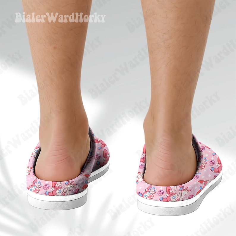 Może przedstawiać: R&oacute;żowe i białe kapcie we wzory z motywem postaci z kresk&oacute;wek. Kapcie mają białą podeszwę i szarą podeszwę środkową. Wz&oacute;r zawiera gwiazdy i inne kształty. Te kapcie są do użytku w pomieszczeniach.