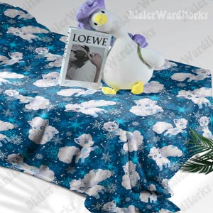 May include: A blue blanket featuring a pattern of white cartoon foxes and snowflakes. A plush goose toy with a purple head and yellow feet rests on the blanket, alongside a book with "LOEWE" on the cover.