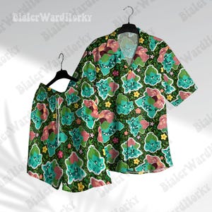 May include: A matching set of green and blue patterned shorts and short-sleeved shirt. The pattern features a cartoon character with pink and yellow floral accents on a dark green background. The shirt and shorts are hanging on black hangers.