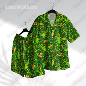 Puede incluir: Conjunto a juego de camisa y pantalón corto con temática de dinosaurios verdes. El conjunto presenta un fondo verde oscuro con un patrón repetido de dinosaurios verdes, detalles amarillos y elementos florales. La camisa tiene mangas cortas y una parte delantera abotonada, mientras que el pantalón corto tiene un cordón.