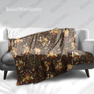 May include: A plush throw blanket featuring a dark brown background with a repeating pattern of stylized yellow fox-like creatures, circular mandala-inspired motifs, and orange cloud shapes. The blanket has a white fleece underside visible at the top.