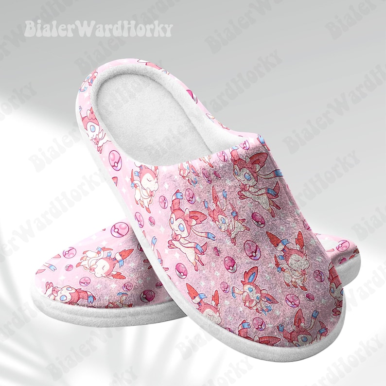 Może przedstawiać: R&oacute;żowe pluszowe kapcie z powtarzającym się wzorem postaci z kresk&oacute;wek z r&oacute;żowymi, białymi i niebieskimi akcentami. Kapcie mają białą podeszwę i miękkie, białe wnętrze. Motyw jest uroczy i zabawny.