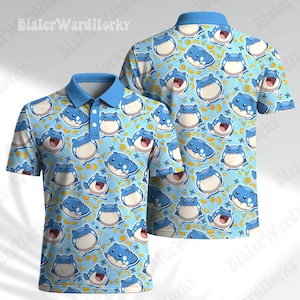 May include: A light blue polo shirt featuring a repeating pattern of cartoon blue and white creatures with open mouths, interspersed with small yellow geometric shapes. The shirt has a solid blue collar and a three-button placket on the front.