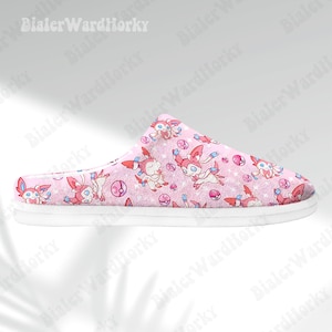 Może przedstawiać: R&oacute;żowa kapcie z białą podeszwą, z powtarzającym się wzorem postaci z kresk&oacute;wek, r&oacute;żowymi i niebieskimi akcentami oraz r&oacute;żowymi i białymi pokeballami. Kapcie są przeznaczone do użytku w pomieszczeniach.