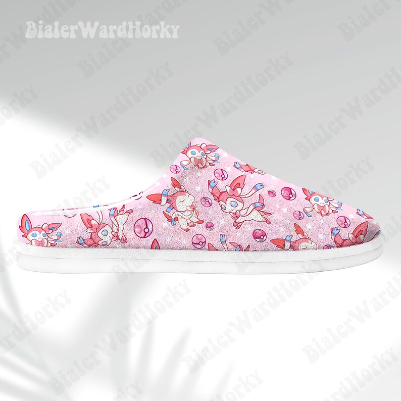 Może przedstawiać: R&oacute;żowa kapcie z białą podeszwą, z powtarzającym się wzorem postaci z kresk&oacute;wek, r&oacute;żowymi i niebieskimi akcentami oraz r&oacute;żowymi i białymi pokeballami. Kapcie są przeznaczone do użytku w pomieszczeniach.