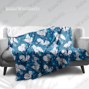 May include: A blue blanket featuring a pattern of white cartoon foxes and snowflakes. The blanket is draped over a grey sofa. The blanket has a soft, plush texture.