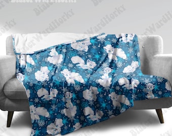 May include: A blue blanket with a pattern of white cartoon foxes and snowflakes. The blanket is draped over a gray sofa. The blanket has a soft, plush texture.