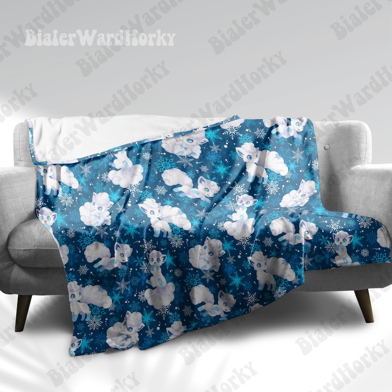 May include: A blue blanket featuring a pattern of white cartoon foxes and snowflakes. The blanket is draped over a grey sofa. The blanket has a soft, plush texture.