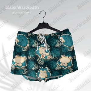 May include: Teal and beige shorts with a pattern of cartoon characters and tropical leaves. The shorts are hanging on a black hanger. The text "Woman Short" is visible at the top.