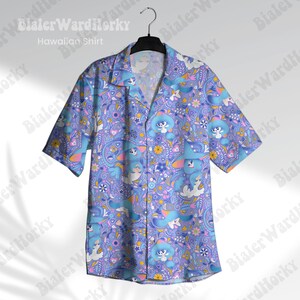 May include: A light blue short-sleeved Hawaiian shirt featuring a playful pattern of cartoon characters, flowers, and paisley motifs. The shirt is suspended from a black hanger. The words "Hawaiian Shirt" are printed on the shirt.