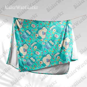 May include: A turquoise blanket featuring a repeating pattern of a sleeping cartoon character, boba tea, strawberries, and avocado slices. The blanket is hanging from a string, with white fabric visible on the edges.