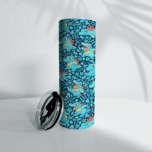May include: A cylindrical tumbler with a teal and navy blue pattern featuring cartoon alligators and floral elements. The tumbler has a black lid and is designed for beverages.