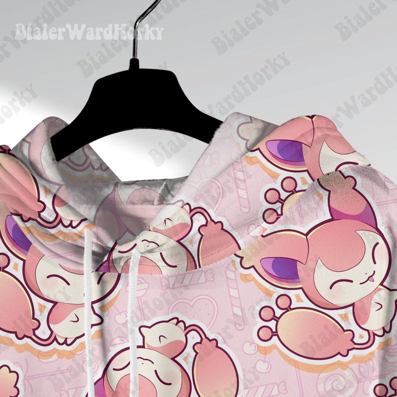May include: A pink hoodie with a repeating pattern of a cartoon character with pink and purple accents. The design includes candy canes, hearts, and other decorative elements on a light pink background. The hoodie is hanging on a black hanger.