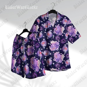 May include: A matching pajama set featuring a short-sleeved button-down shirt and shorts. The set is navy blue with a repeating pattern of purple cartoon characters with white cloud accents. The shorts have a white drawstring.