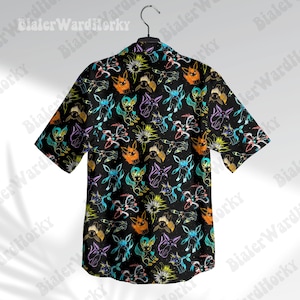 Puede incluir: Camisa negra de manga corta con un colorido estampado de personajes de dibujos animados. La camisa est&aacute; colgada de una percha. El estampado incluye personajes en naranja, azul, morado y amarillo.