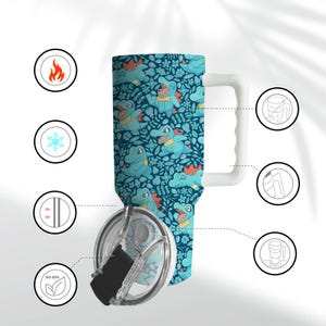 May include: A teal travel mug with a white handle and lid. The mug is decorated with a pattern of cartoon alligators and flowers. The lid is clear with a black slider. The mug has a capacity of approximately 887 ml.