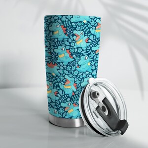 May include: A stainless steel travel mug with a teal and blue pattern of cartoon alligators and floral designs. The lid is clear with a black handle. The mug is suitable for hot or cold drinks.