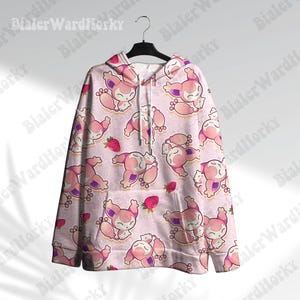 May include: A light pink hoodie with a repeating pattern of cartoon characters and strawberries. The characters are primarily pink and white with purple accents. The hoodie has a drawstring and is hanging on a black hanger.