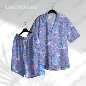 Puede incluir: Un conjunto de pijama a juego con una camisa de manga corta y pantalones cortos. El conjunto presenta un diseño caprichoso en tonos azules, morados y blancos, con personajes de dibujos animados y elementos florales.
