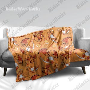 May include: An orange blanket featuring a repeating pattern of cartoon dragons in various poses. The dragons are primarily red and orange with white accents. The blanket is draped over a gray sofa.