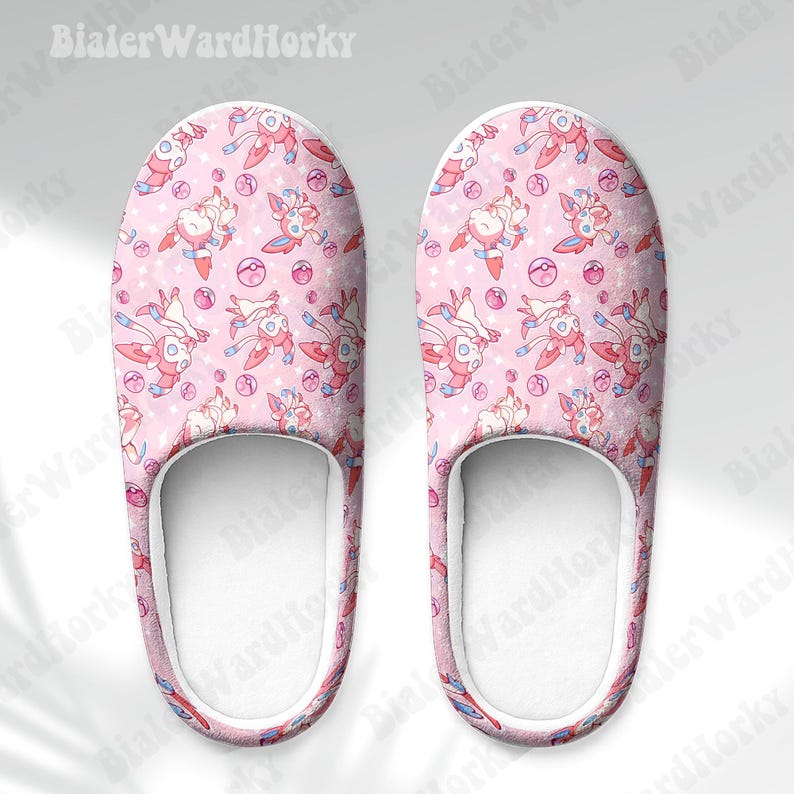 Może przedstawiać: Para r&oacute;żowych kapci z powtarzającym się wzorem postaci z kresk&oacute;wek, gwiazd i r&oacute;żowych i fioletowych kul. Kapcie mają białe wnętrze i niebiesko-czerwone wykończenie. Tekst "BialerWardHorky" jest widoczny u g&oacute;ry.