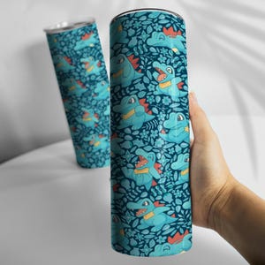 May include: A teal insulated tumbler with a repeating pattern of cartoon alligators, flowers, and leaves. The alligators have orange and yellow accents. The background is a dark teal colour. The tumbler is cylindrical and has a silver lid.