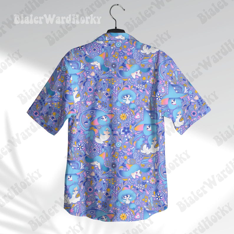 May include: Short-sleeved shirt with a button-down collar, displaying a playful pattern. The design includes cartoon characters in blue, white, and pink, set on a lavender paisley backdrop. The shirt is suspended from a metal hanger.
