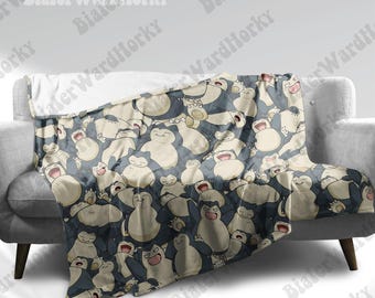 May include: A soft, beige and blue throw blanket with a repeating pattern of cartoon Snorlax characters. The blanket is made of a soft, plush material and is perfect for cuddling up on the couch.