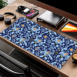 May include: A rectangular desk mat featuring a repeating pattern of blue, muscular, four-armed cartoon characters with yellow accents, interspersed with stylized yellow flowers, dark blue leaves, and small grey circular shapes on a dark blue background.