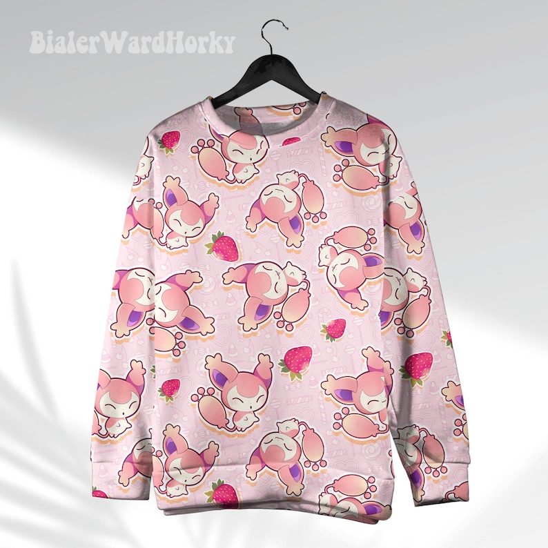 May include: Pink sweatshirt with a repeating pattern of cartoon characters and strawberries. The characters are pink and white with purple accents. The strawberries are red. The sweatshirt is hanging on a black hanger.