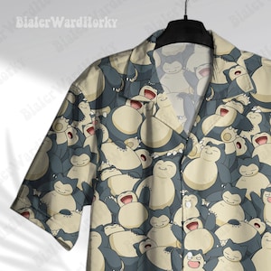 May include: A short-sleeved button-down shirt featuring a repeating pattern of a cartoon character in shades of blue, cream, and white. The shirt is hanging on a black hanger. The shirt's design is visible on the collar and sleeves.