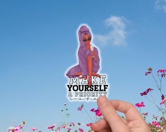 May include: A sticker with the text "MAKE YOURSELF A PRIORITY" featuring an illustration of a person in a purple robe and towel, holding a champagne glass. The sticker is held in front of a field of flowers and a blue sky.