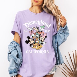 May include: Purple t-shirt with a white graphic of Mickey Mouse and friends. The graphic says "Disneyland Est. 1955 California".