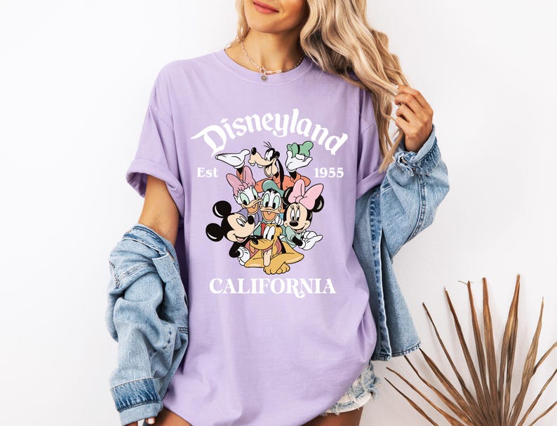 May include: Purple t-shirt with a white graphic of Mickey Mouse and friends. The graphic says "Disneyland Est. 1955 California".