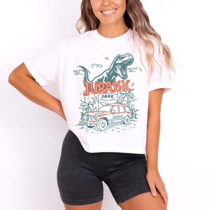 Pu&ograve; includere: Una t-shirt bianca a maniche corte con una stampa grafica di un dinosauro T-Rex, una scena nella giungla e un veicolo con la scritta Jurassic Park in inchiostro rosso e verde. La maglietta &egrave; abbinata a pantaloncini neri a coste testurizzati.