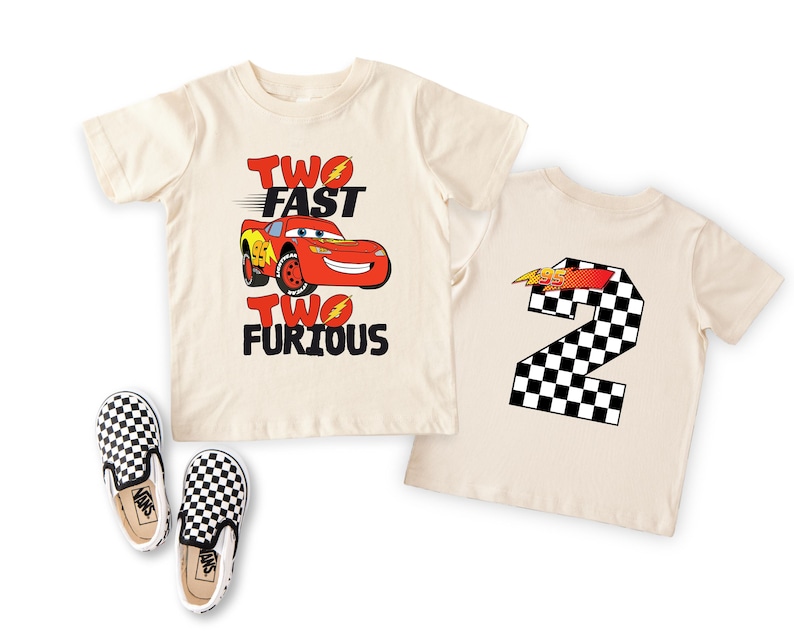 May include: Two cream-colored short-sleeve t-shirts and a pair of black and white checkered slip-on shoes. One shirt features a red race car graphic with the text TWO FAST TWO FURIOUS. The other shirt displays a large checkered number 2.