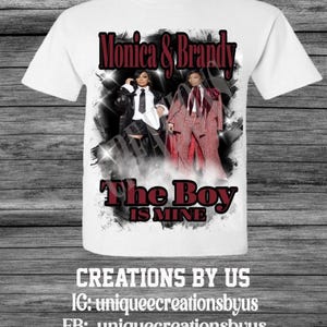 Pode incluir: Camiseta branca com um gráfico de duas mulheres e o texto "Monica & Brandy" acima e "The Boy Is Mine" abaixo. A camiseta também inclui as redes sociais de "Creations By Us".