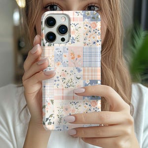 May include: A smartphone case featuring a patchwork design of soft pastel colors. The pattern consists of alternating squares with floral prints in shades of peach, light blue, and white, interspersed with light orange and blue checkered squares.
