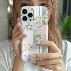 Puede incluir: Una funda para teléfono con un diseño de patchwork que presenta patrones florales y una variedad de colores, incluyendo rosa, verde y blanco.