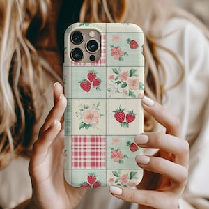 May include: A white phone case with a patchwork design featuring strawberries, flowers, and a pink and white plaid pattern.