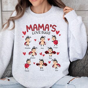 May include: Gray sweatshirt with the text "Mama's Love Bugs" and a design of red ladybugs with names underneath each one. The names are Sebastian, Andy, Cooper, Brandon, Nora, Hannah, Evelyn, and Eliza.