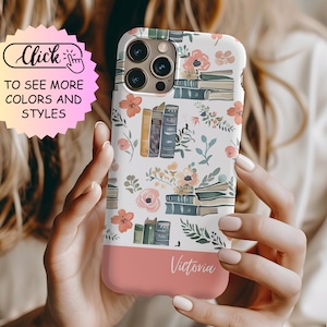 May include: A white smartphone case featuring a repeating pattern of stacked books, green leaves, and coral-colored flowers. The bottom section is a solid coral color with the name Victoria printed in white script. The case has a camera cutout.