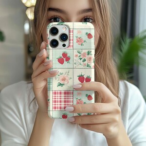 May include: A white iPhone case with a patchwork design featuring strawberries, flowers, and a red and white gingham pattern.