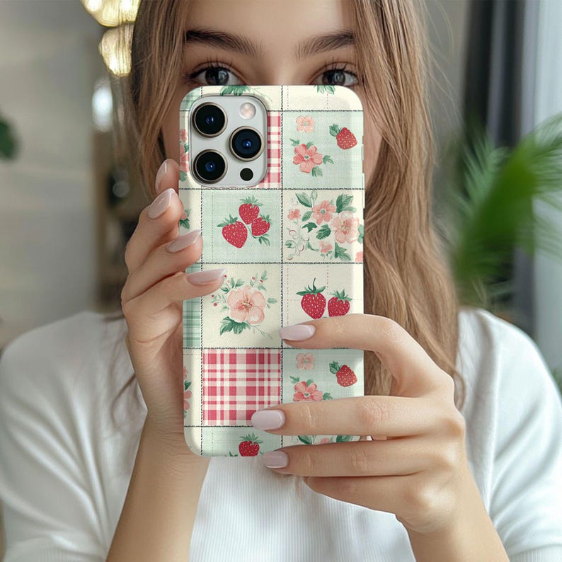 May include: A white iPhone case with a patchwork design featuring strawberries, flowers, and a red and white gingham pattern.