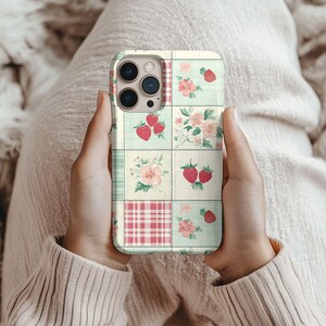 May include: A phone case with a patchwork design featuring pink and green squares with floral and strawberry patterns.