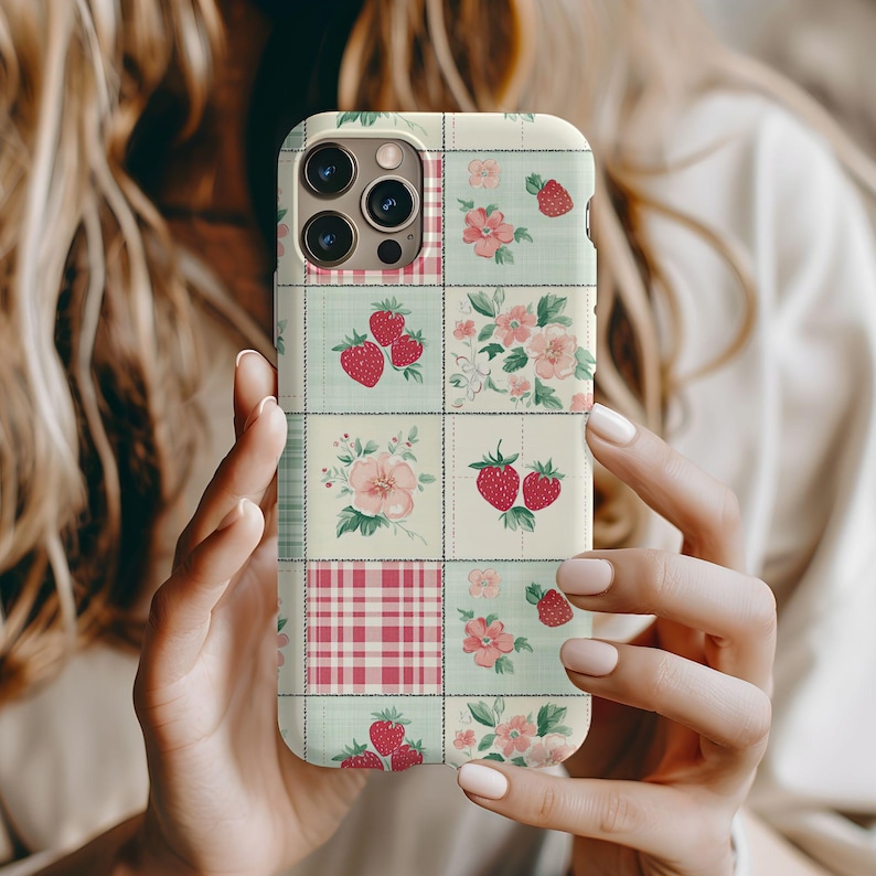 May include: A white phone case with a patchwork design featuring strawberries, flowers, and a pink and white plaid pattern.