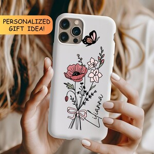 May include: A white phone case featuring a black-lined illustration of a bouquet of pink flowers tied with a bow, a small black and pink butterfly, and the name Lilianna written in black script. The case has a cutout for a triple camera system.