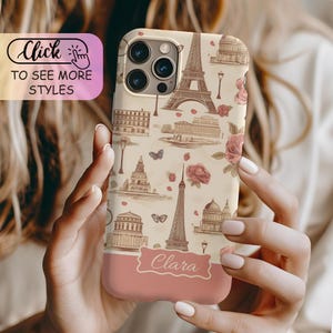 May include: A beige smartphone case featuring a repeating pattern of brown line-art illustrations of the Eiffel Tower, Parisian buildings, butterflies, and pink roses. A solid pink horizontal banner at the bottom displays the name Clara in white.